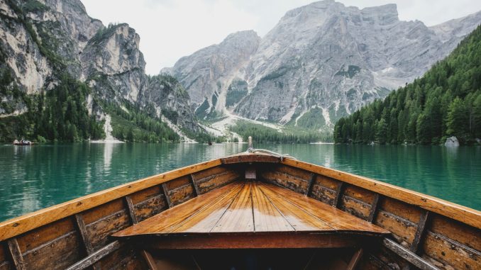 Photo by Luca Bravo brown wooden boat moving towards the mountain