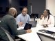 a group of people sitting around a table with laptops