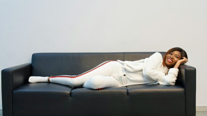 Photo by Joyce Busola woman in white long sleeve shirt lying on black couch
